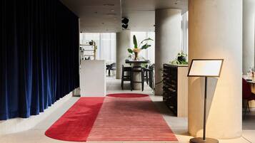 A hotel lobby with a red carpet, dark blue curtains, a reception desk, and a plant.