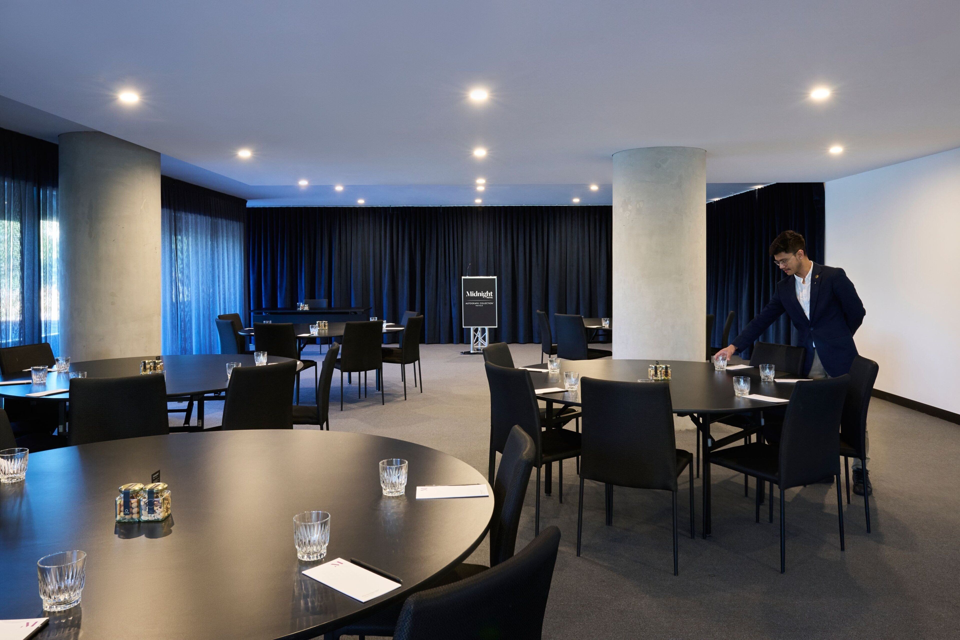 A modern conference room with round tables, black chairs, and a podium.