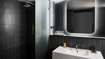 A modern bathroom with a large mirror, a shower, and a sink with toiletries.
