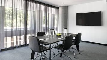 Uma sala de conferências com uma mesa grande, quatro cadeiras, uma TV de tela plana e um grande janela com cortinas translúcidas.