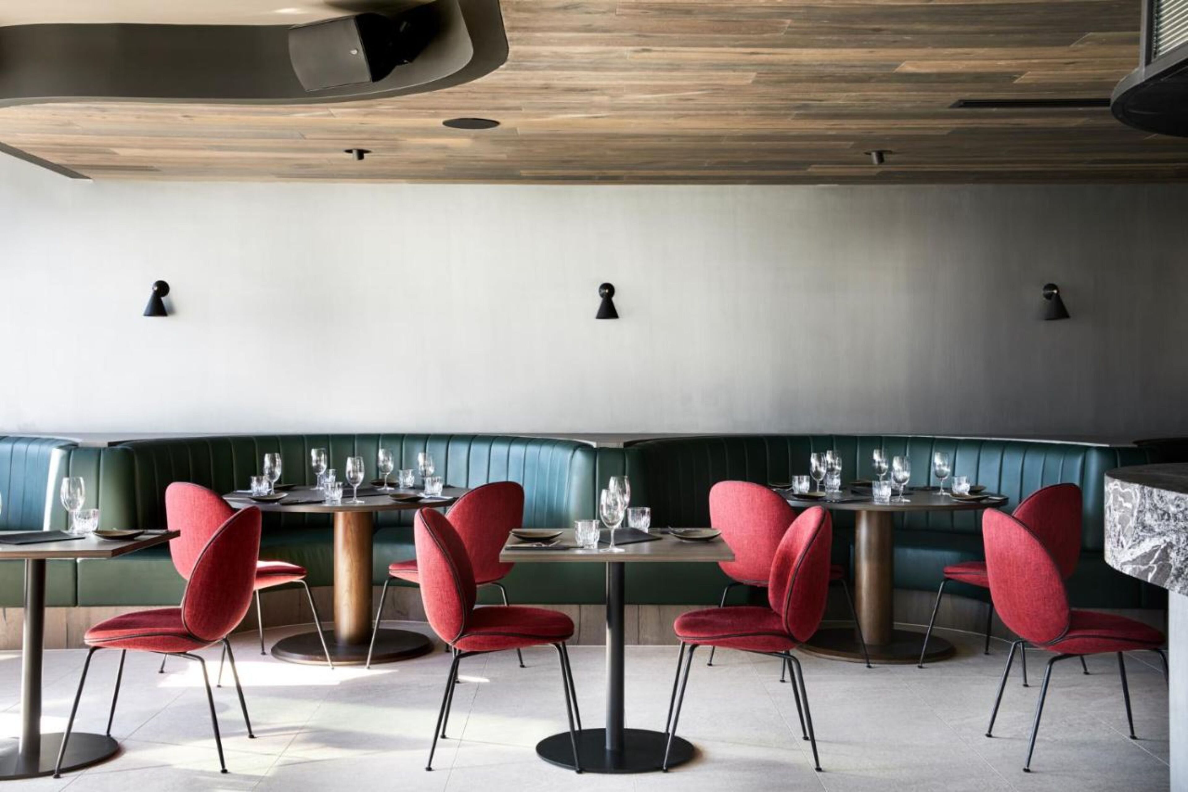 A restaurant with green booths and red chairs, wooden ceiling, and pendant lighting.