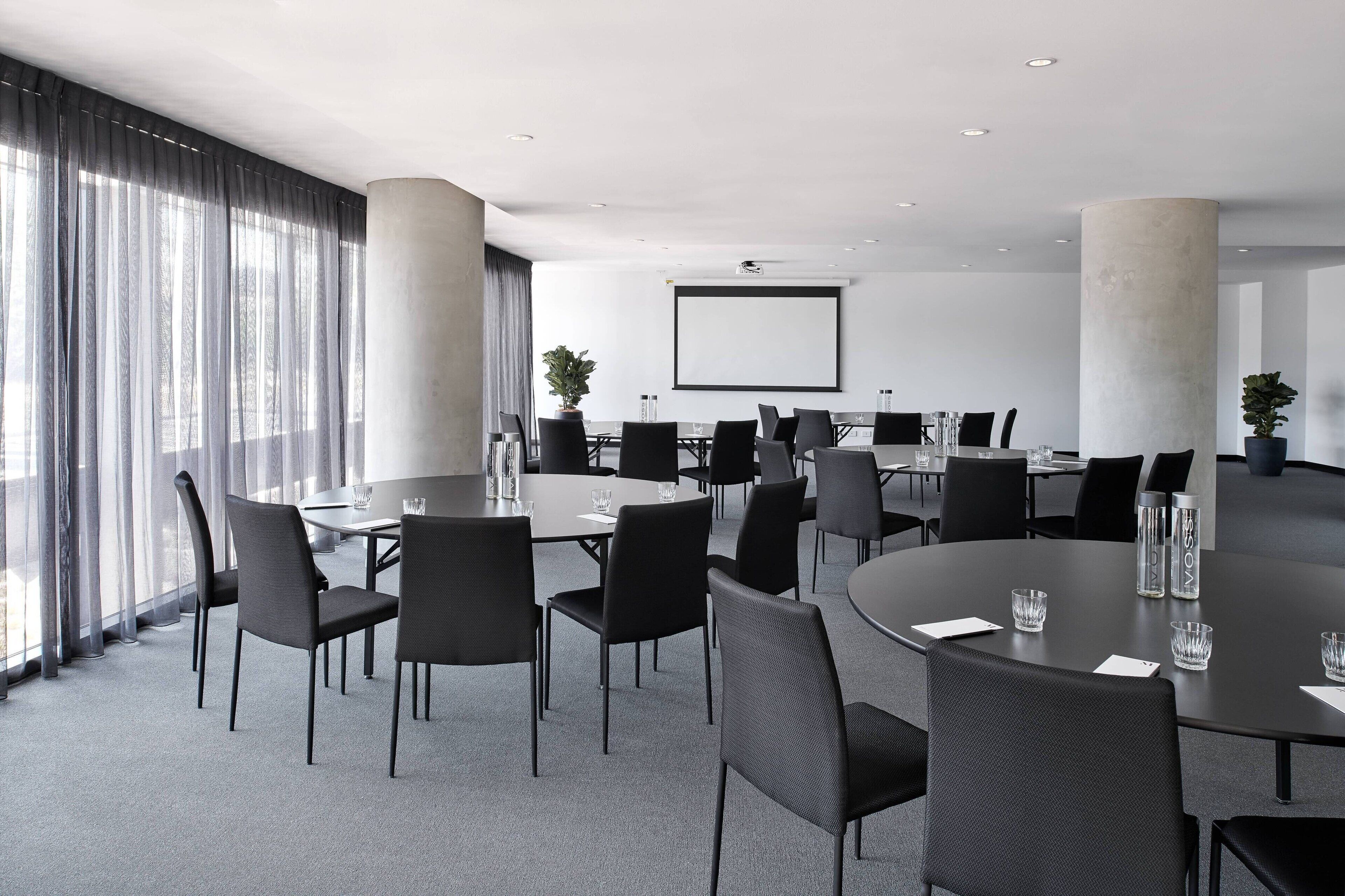 A modern conference room with round tables, black chairs, and a large screen.