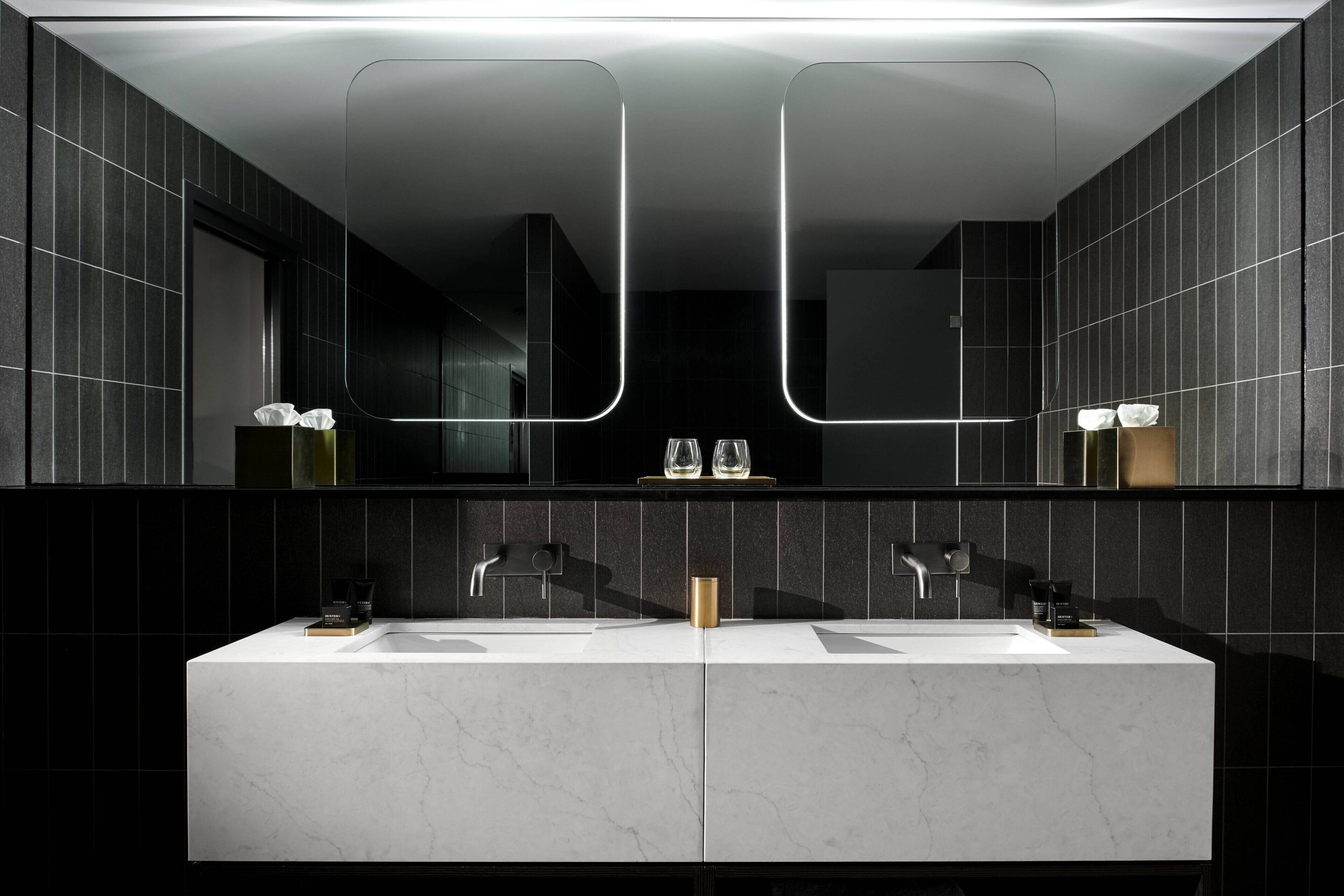 A modern bathroom with two sinks, a large mirror, and a gold accent piece.
