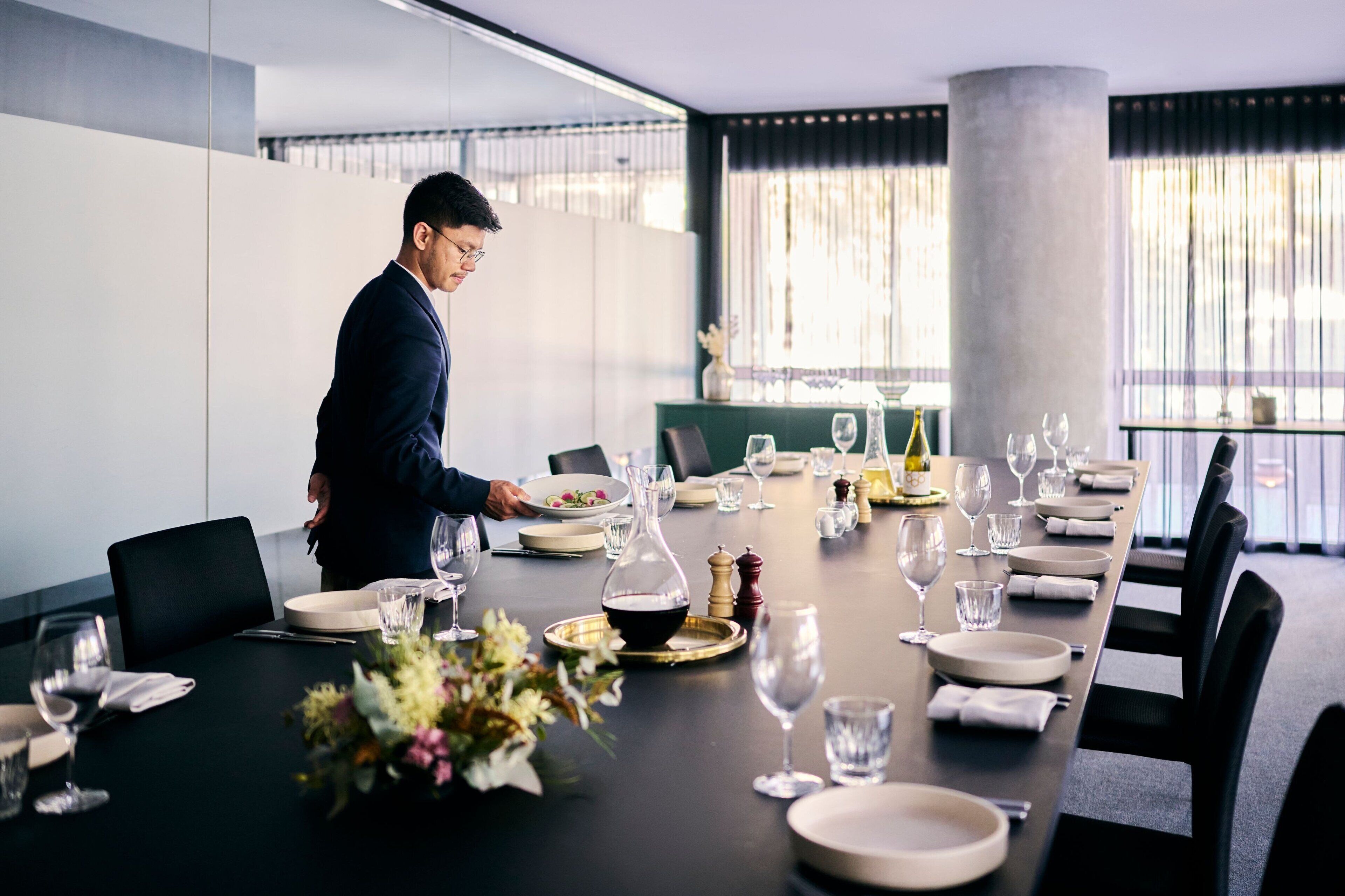 A conference room with a long table set for a meeting, featuring a modern design with a neutral color palette.