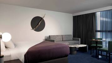 Una habitación de hotel moderna con una cama grande, un sofá, una mesa de centro y una mesa de comedor con sillas.