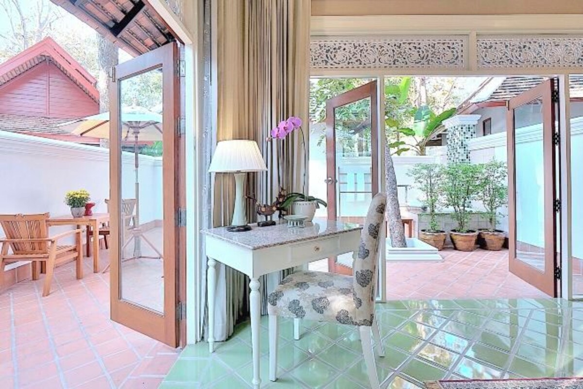 A room with a desk, chair, and a large mirror. There is a window with a view of the outside.