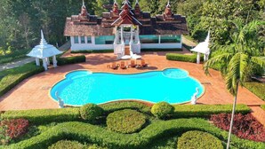 A large swimming pool surrounded by manicured gardens and a traditional building with multiple spires. - MonPanaNont Wellness Resort & Spa (Mae Taeng)