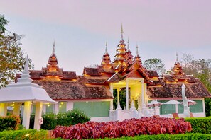 A traditional multi-tiered temple with a central entrance, surrounded by well-maintained gardens and a white pavilion.