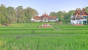 A traditional building with multiple spires, surrounded by lush green fields and trees. - MonPanaNont Wellness Resort & Spa (Mae Taeng)