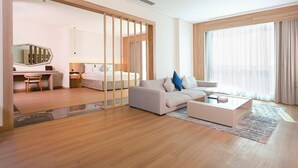 Una habitación de hotel moderna con suelo de madera, sofá, cama, escritorio y un ventanal con cortinas.