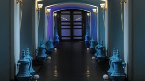 Un pasillo iluminado en azul con un arco, apliques decorativos y jarrones ornamentales azules a lo largo de las paredes.