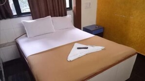 A neatly made bed with a brown bedspread and white pillows, a remote control, and a folded white towel on the bed. - Summerland Guest House (Mumbai)