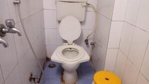 A small, narrow bathroom with a white toilet and a yellow seat cover. - Summerland Guest House (Mumbai)