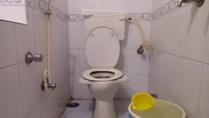 A small, basic bathroom with a toilet, a yellow bucket, and a white bucket on the floor. - Summerland Guest House (Mumbai)