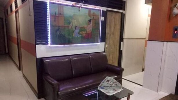 A lobby with a leather sofa, a glass coffee table with a newspaper, and a wall-mounted TV displaying a scene. - Summerland Guest House (Mumbai)