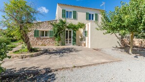 Una casa de dos pisos con fachada de piedra, contraventanas verdes y un camino de entrada de grava.