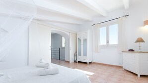 Un dormitorio con cama, armario, ventana con cortinas y baño visible a través de un arco.