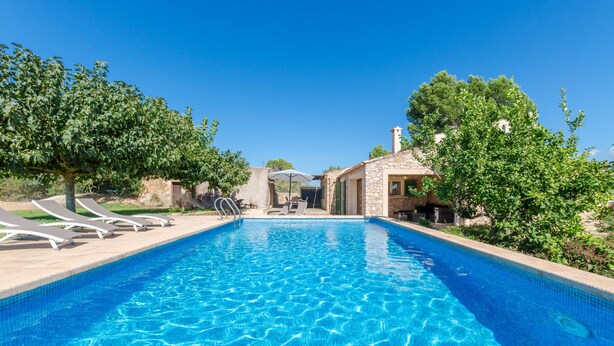 Una piscina con sillones de descanso y un edificio de piedra al fondo.