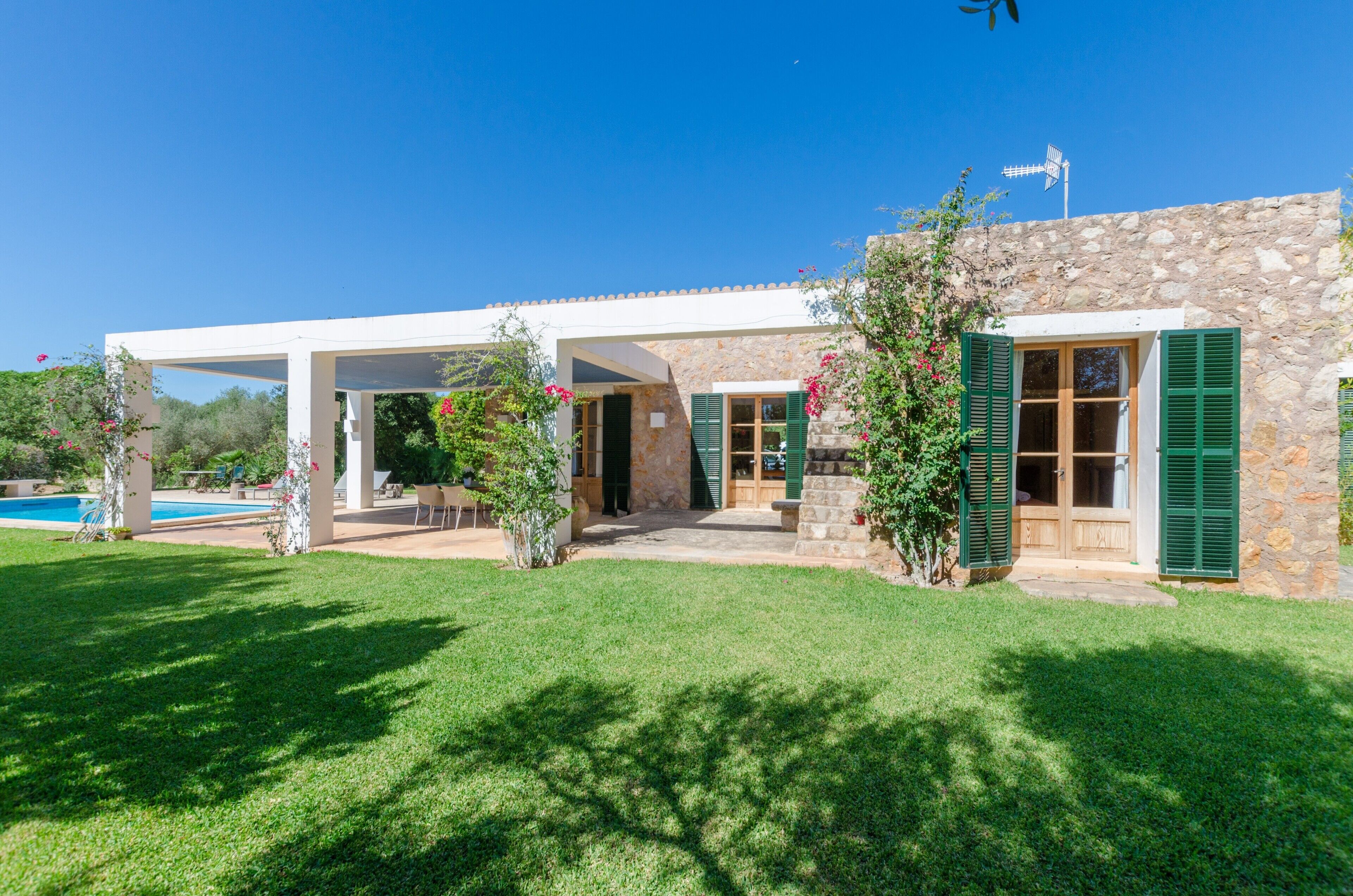 A stone building with a covered patio, a pool, and green shutters.