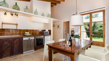 A kitchen with wooden cabinets, a dishwasher, a microwave, and a dining table with chairs. There is a window with a view of greenery outside.