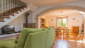 Una sala de estar con un sofá verde, un televisor, un comedor con una mesa y sillas, y una escalera con barandillas de madera.