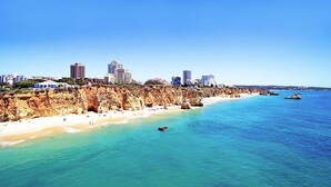 Un paisaje urbano costero con playa arenosa, acantilados rocosos y edificios altos.