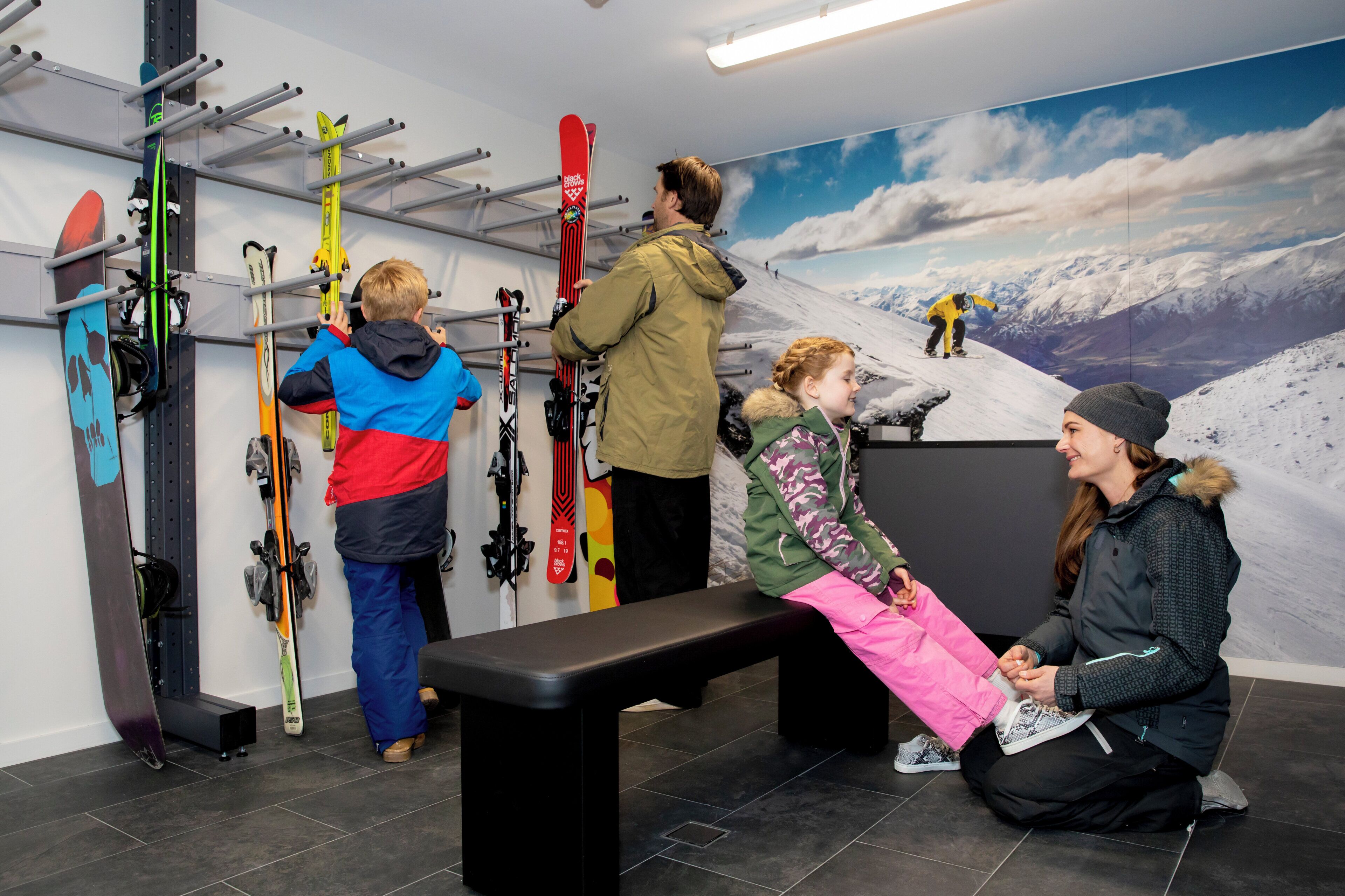A ski rental area with multiple skis and snowboards, a bench, and a large wall mural of a snowy mountain.