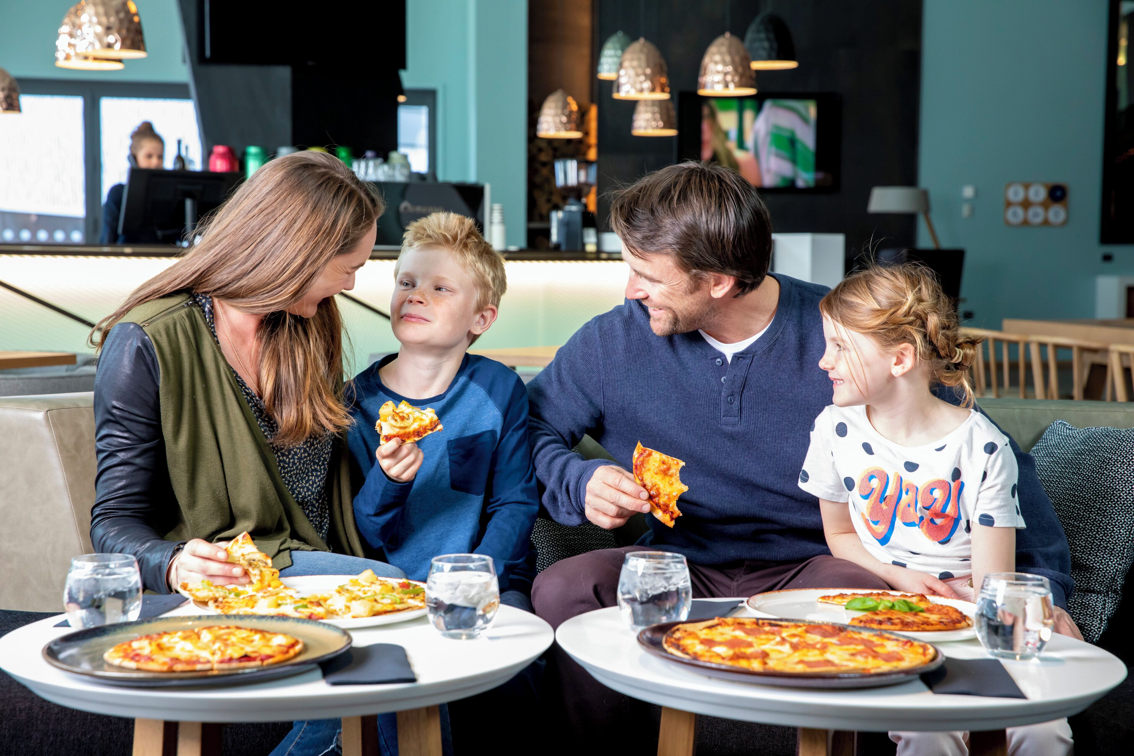 A family dining at a restaurant with pizza and water glasses on the table.