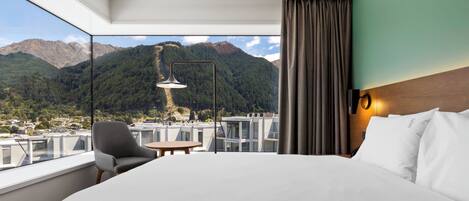 A hotel room with a large bed, a chair, a small table, and a view of mountains.