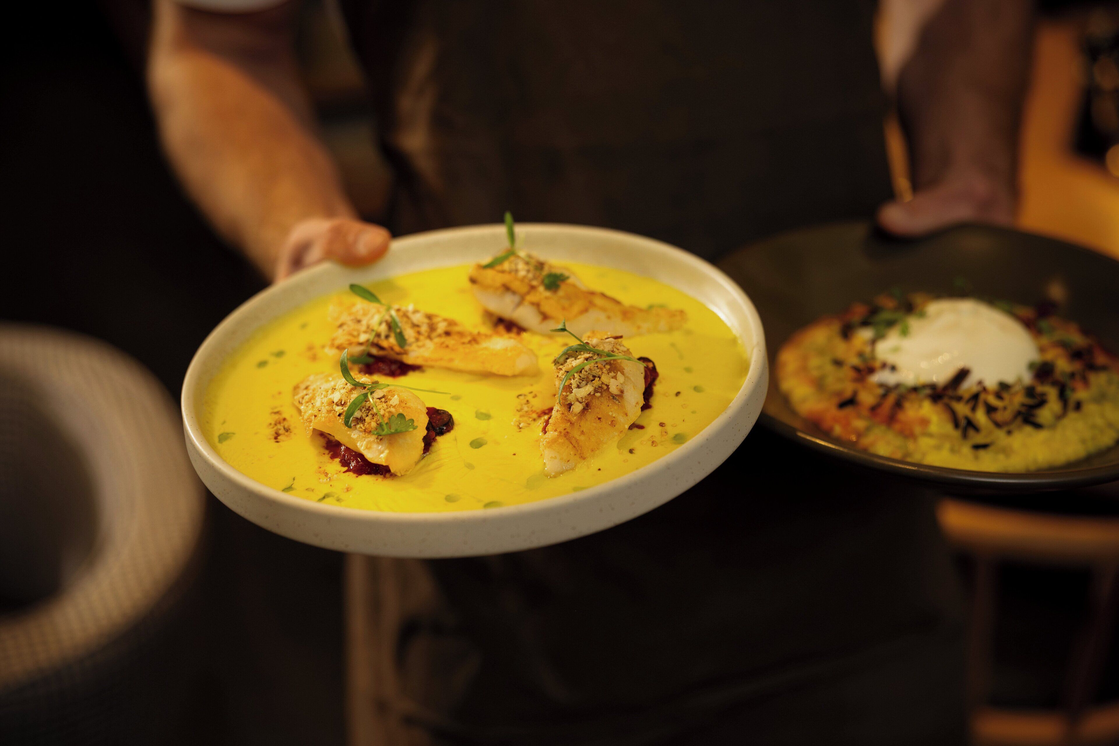 A person holding a plate with a yellow dish and a side dish.
