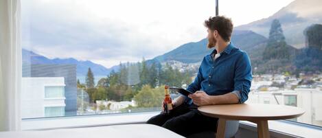 A person sitting at a table by a window with a view of mountains and buildings.