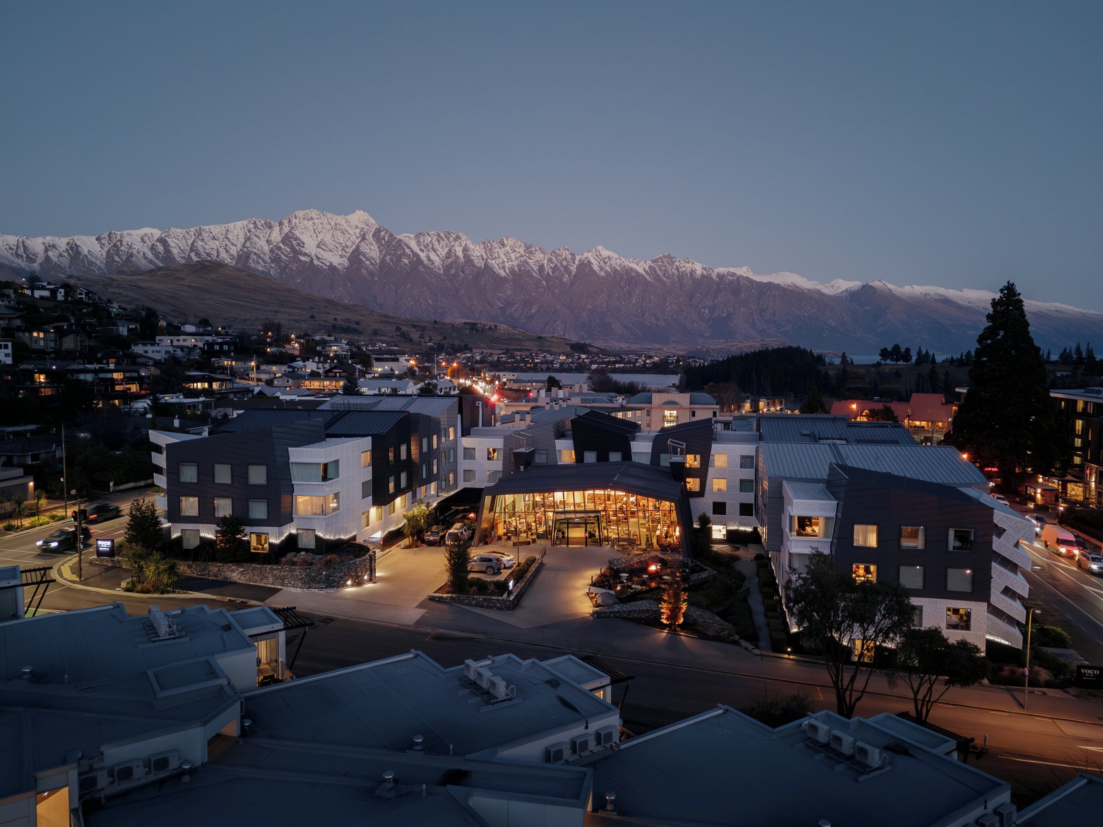Um hotel moderno com um pátio central, rodeado por edifícios residenciais, e uma cordilheira ao fundo.