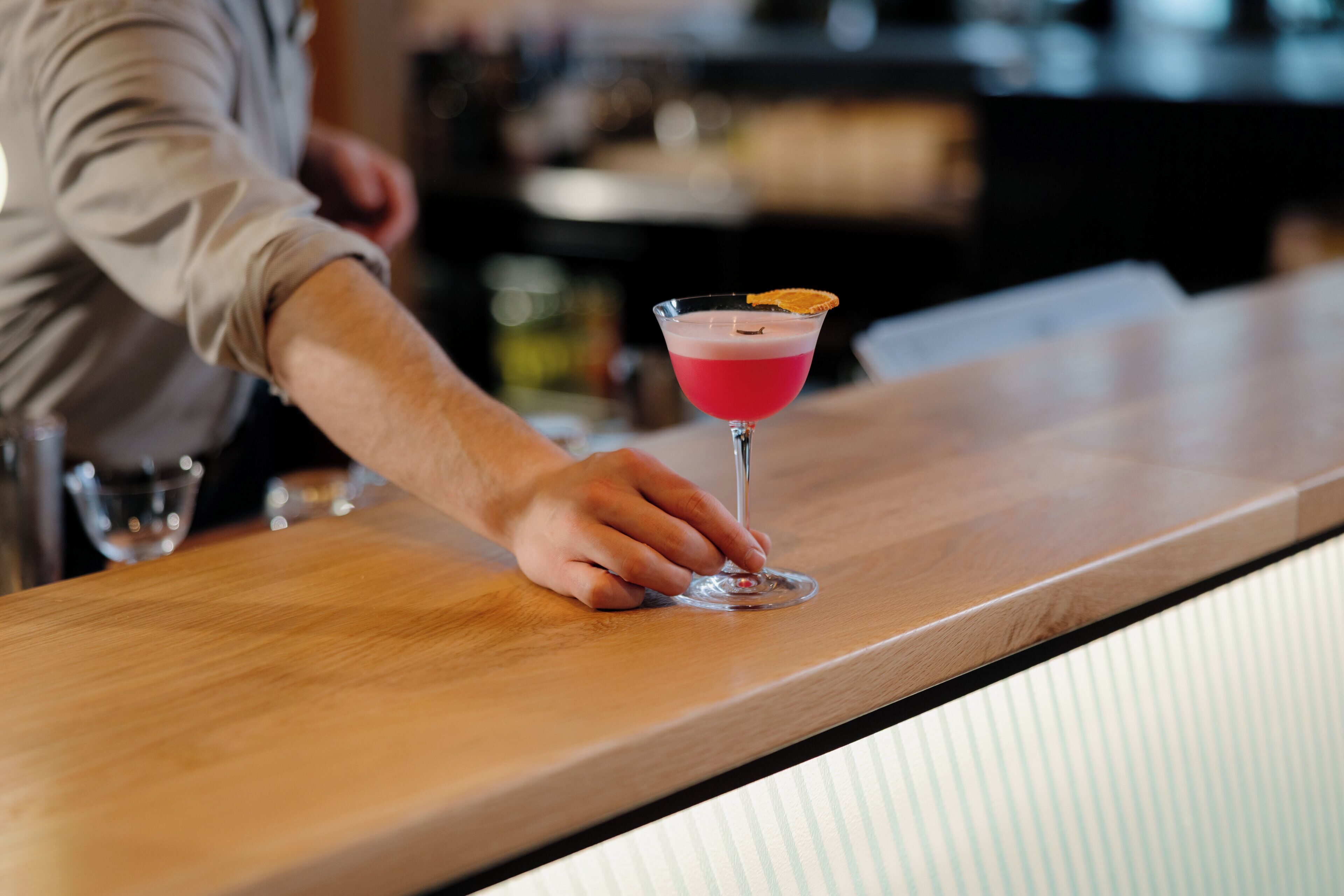 A bartender placing a glass on a bar counter.