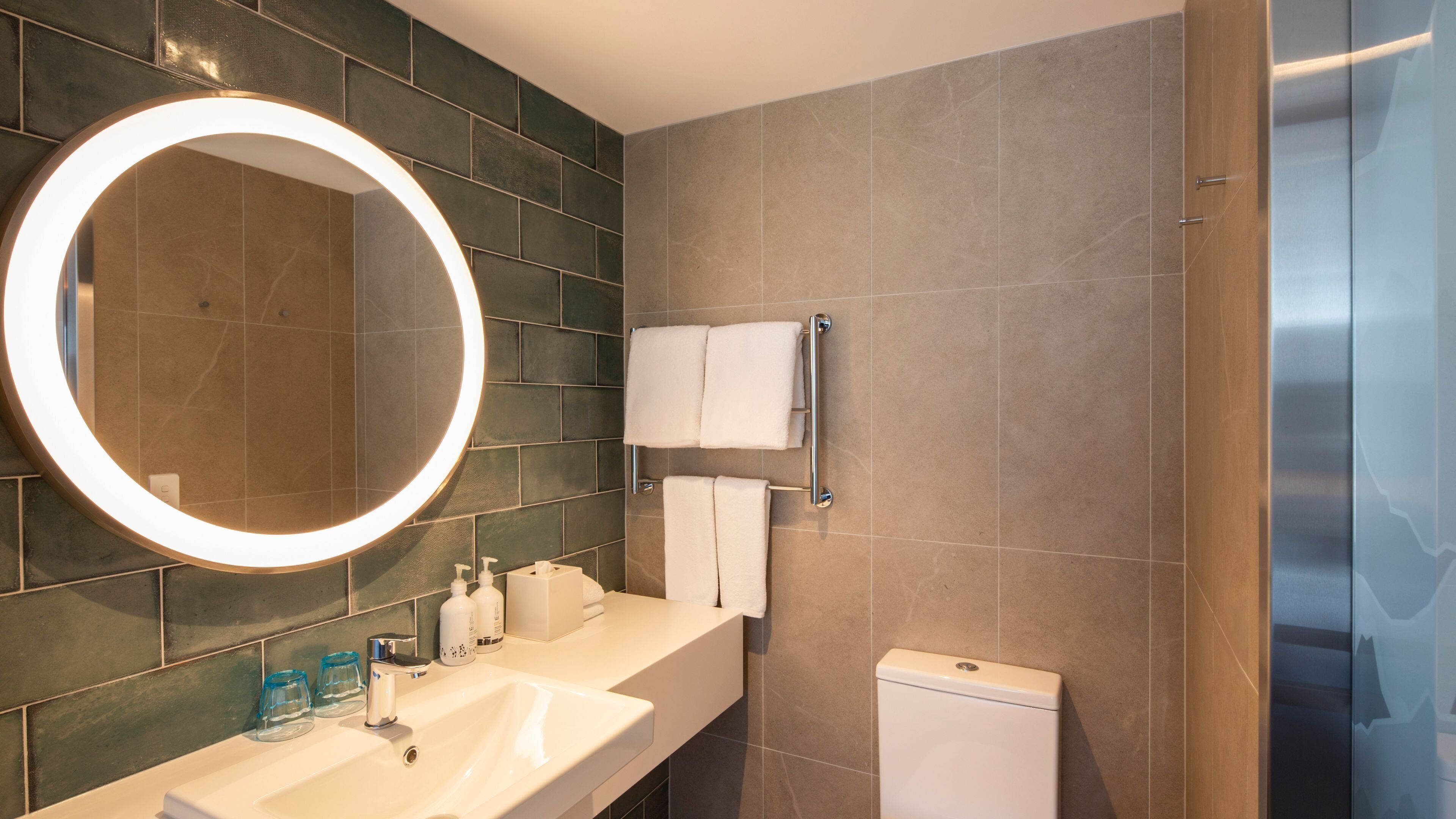 Une salle de bain moderne avec un grand miroir, un lavabo, des toilettes et un porte-serviettes.