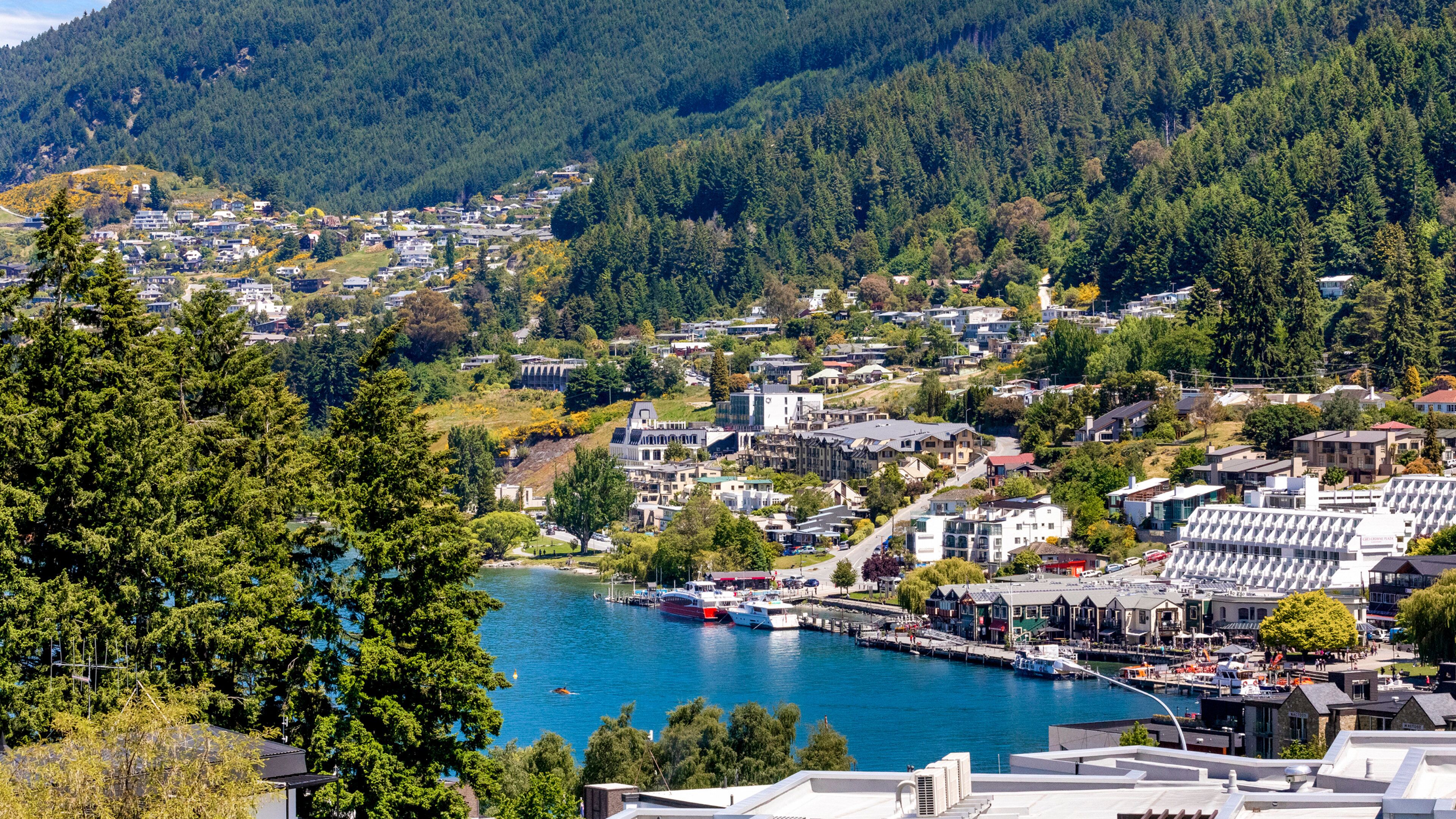 A coastal town with a marina, residential buildings, and a backdrop of forested hills.