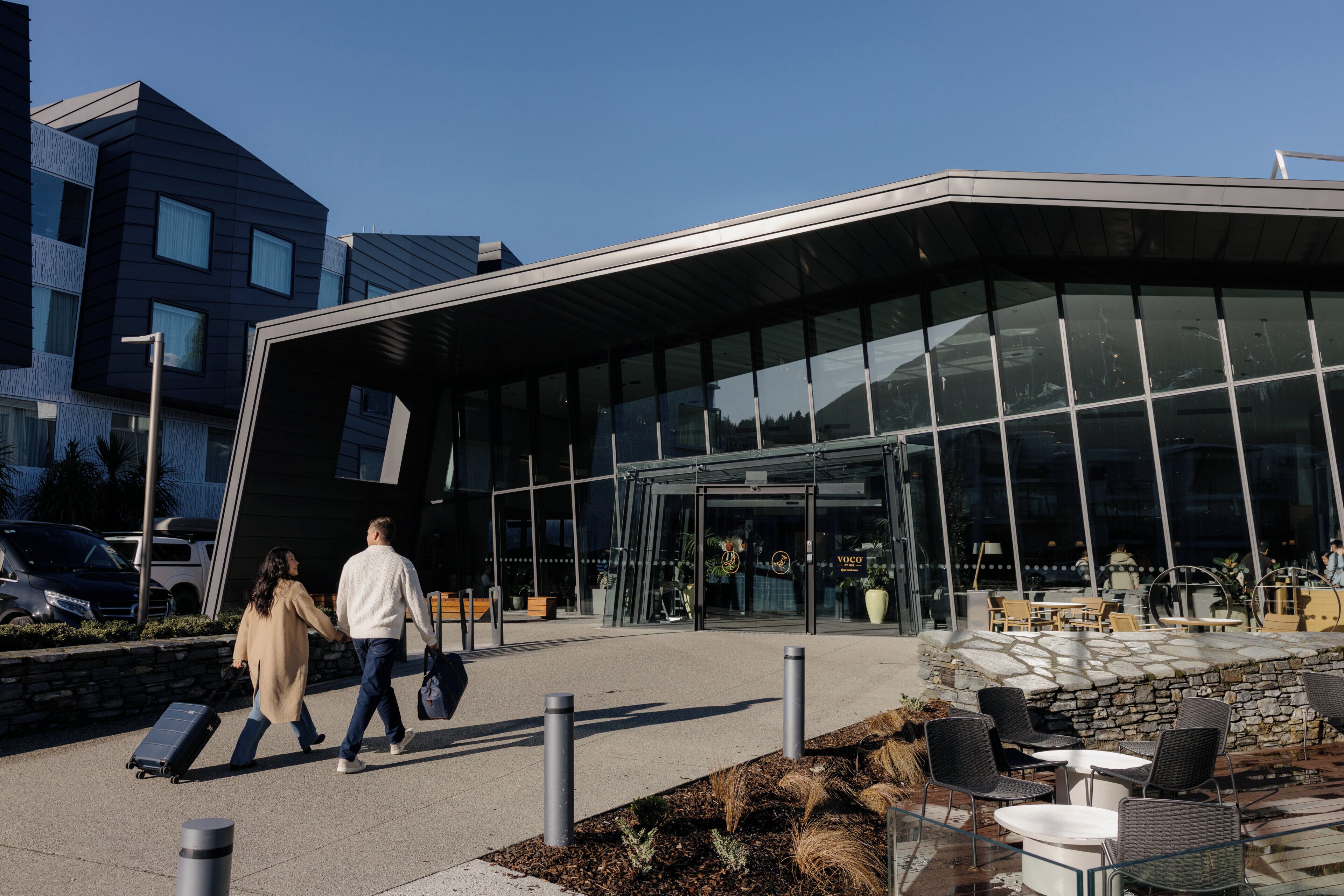 A modern building with a glass facade, outdoor seating area, and a clear sky.