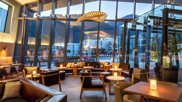 A modern interior with large windows, comfortable seating, and a central light fixture. - voco Queenstown by IHG (Queenstown)