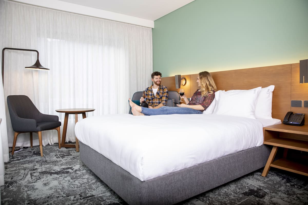 A hotel room with a large bed, a small table, a chair, and a lamp.