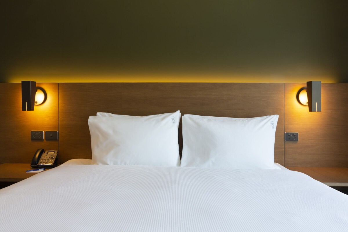 A hotel room with a large bed, two bedside tables, a phone, and wall-mounted lighting.
