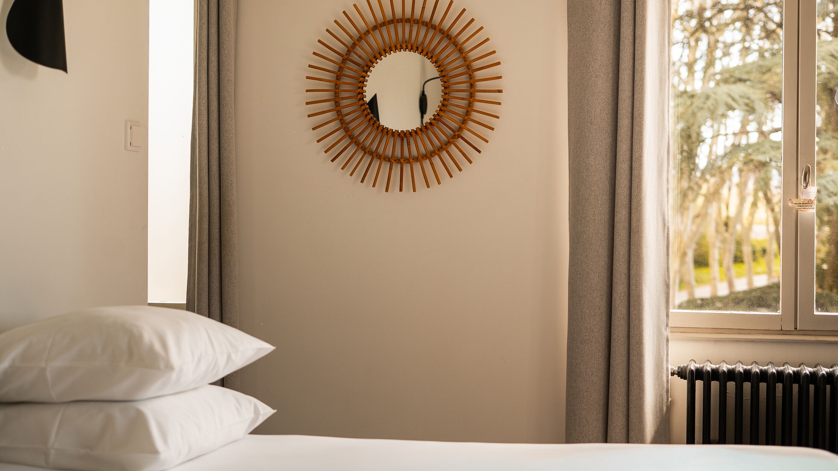 A bedroom with a bed, a wall-mounted mirror, a window with curtains, and a radiator.
