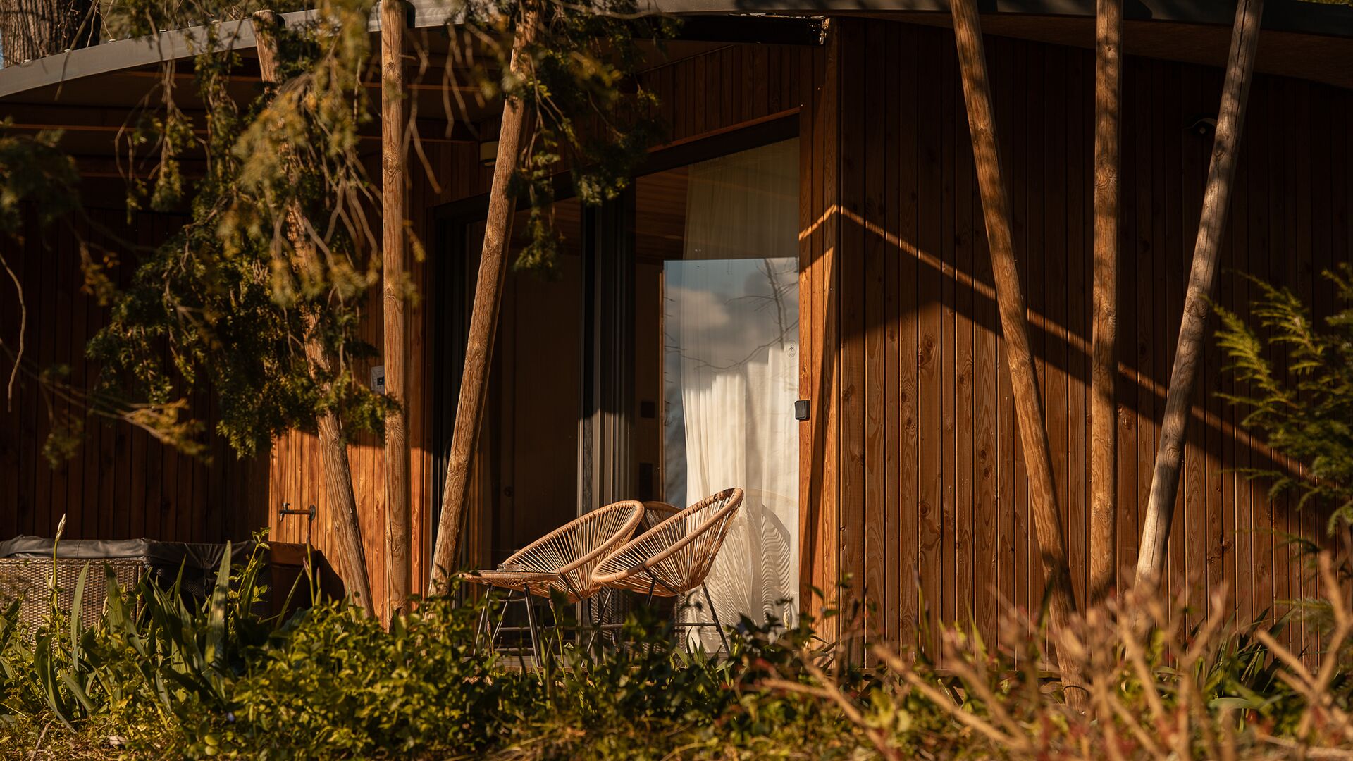 A wooden building with a door, two wicker chairs outside, and vegetation in front.