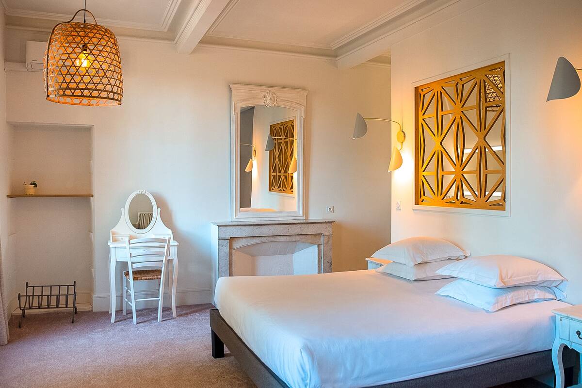 A bedroom with a bed, a chair, a dresser, a mirror, and a wall-mounted light fixture.
