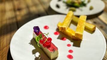 Une assiette à dessert avec un gâteau à plusieurs couches, des baies et une fleur, le tout posé sur une table en bois.