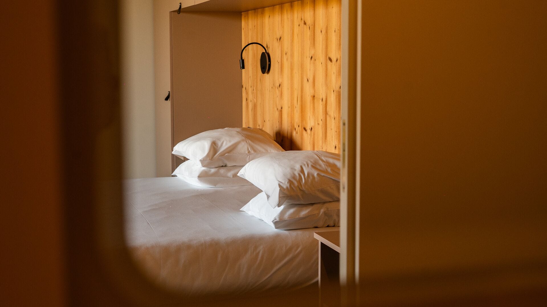 A bed with white bedding, a wooden headboard, and a wall-mounted headphone jack.