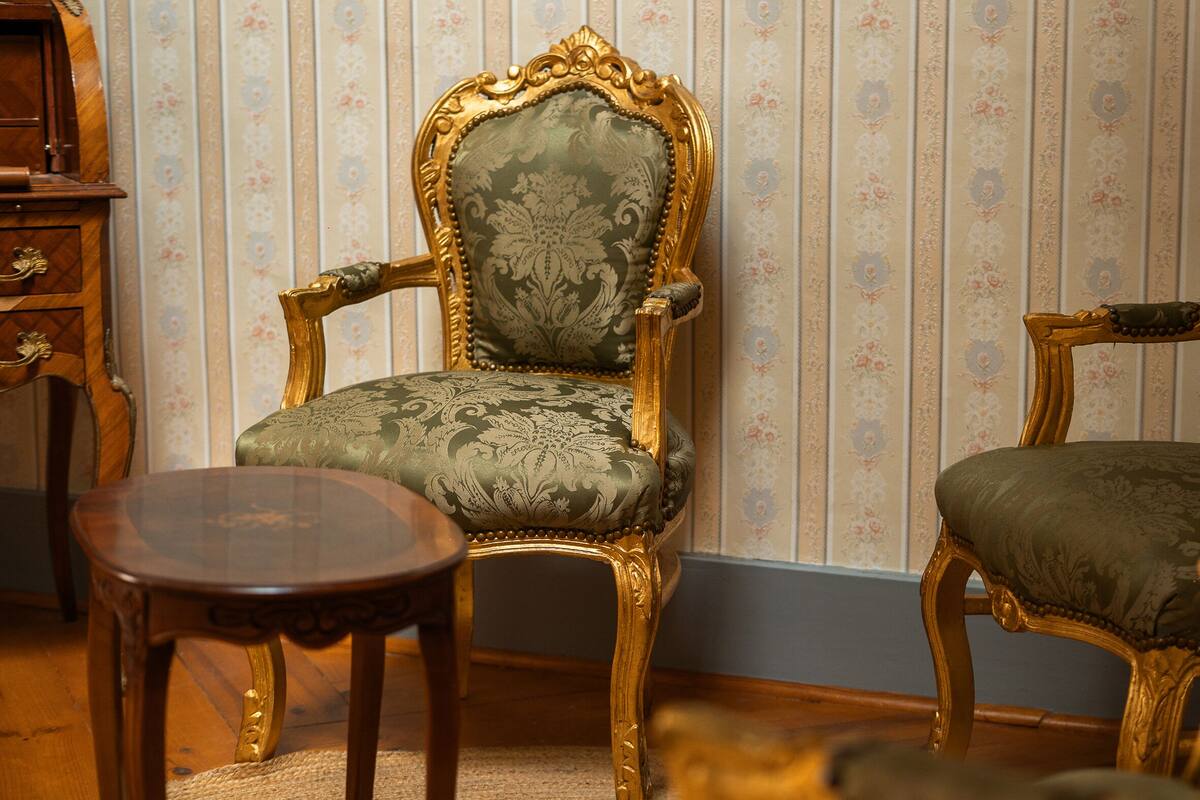 A room with two ornate chairs, a small wooden table, and a patterned wallpaper background.