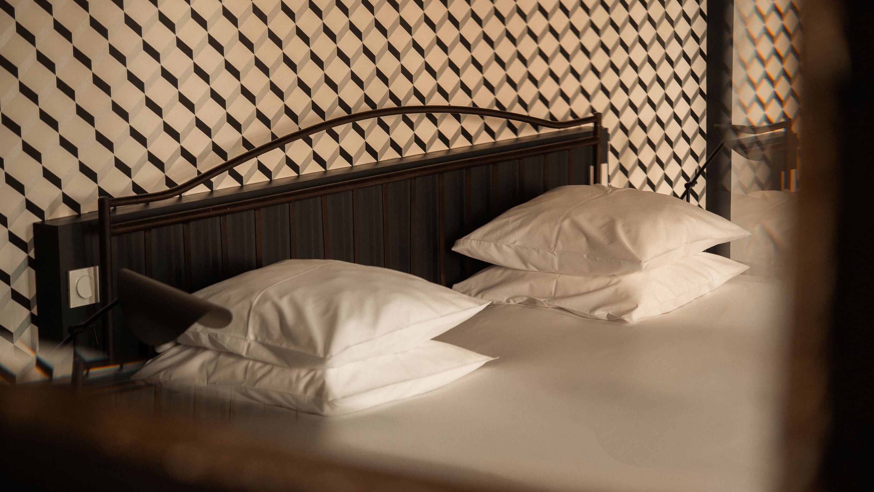 A bed with a wooden headboard, white pillows, and a patterned wall.
