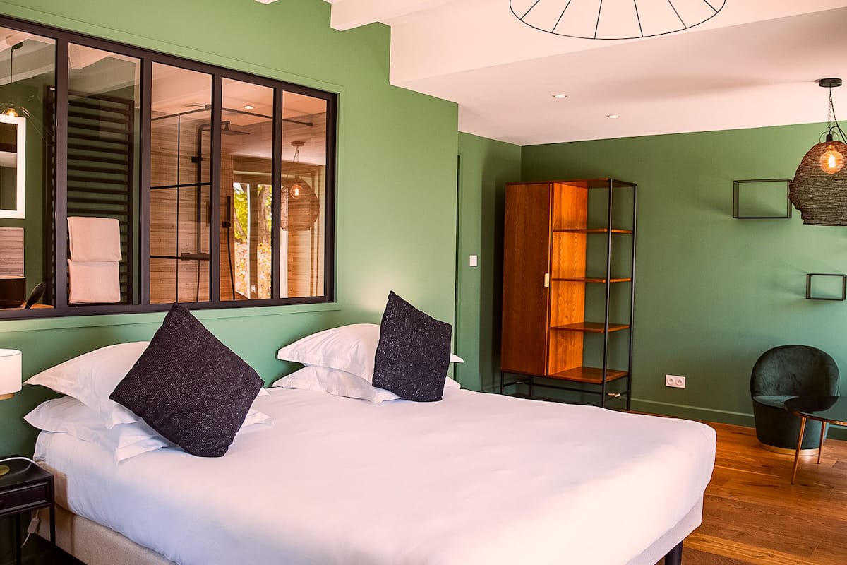 A hotel room with a large bed, a wooden wardrobe, a small table, and a chair.
