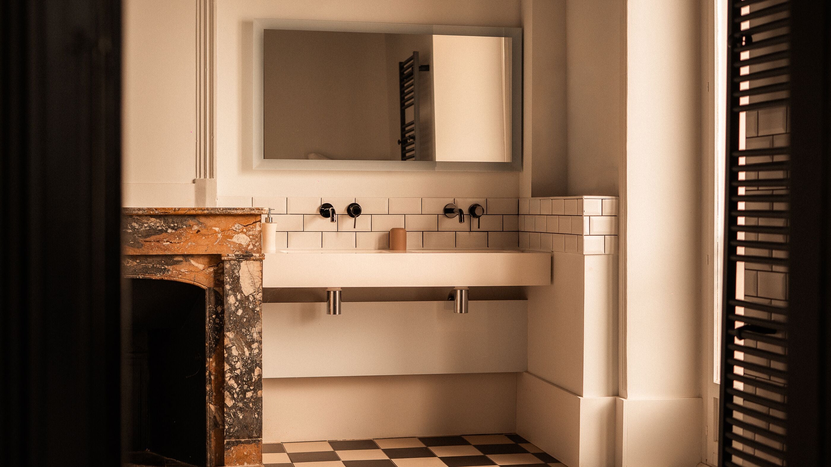 Une salle de bain avec une cheminée en marbre, un lavabo blanc et un miroir au-dessus.