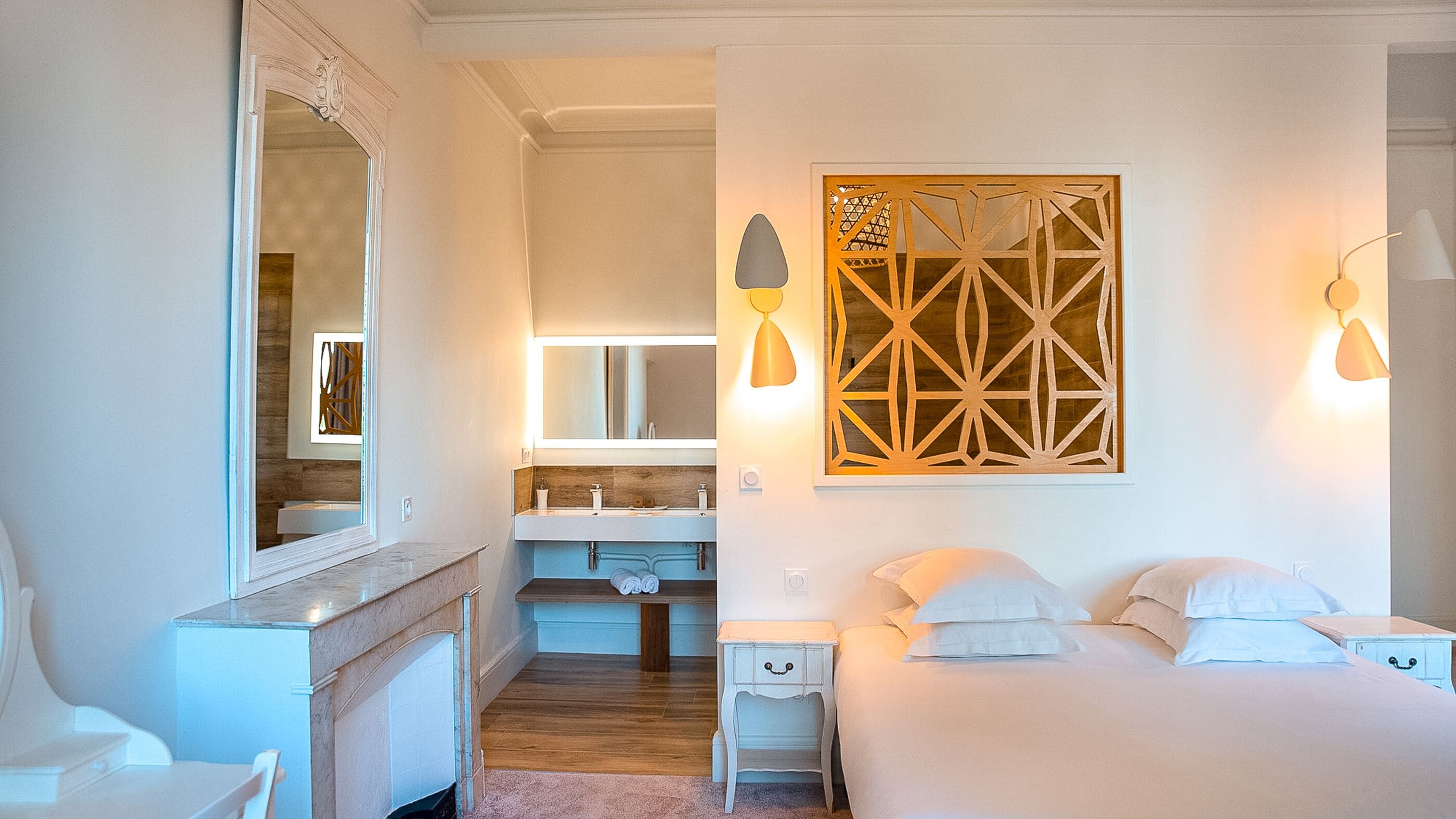 Une chambre d’hôtel avec un grand miroir, un décor mural en bois, un lit avec des oreillers, une table de chevet et une salle de bain avec un lavabo et un miroir.