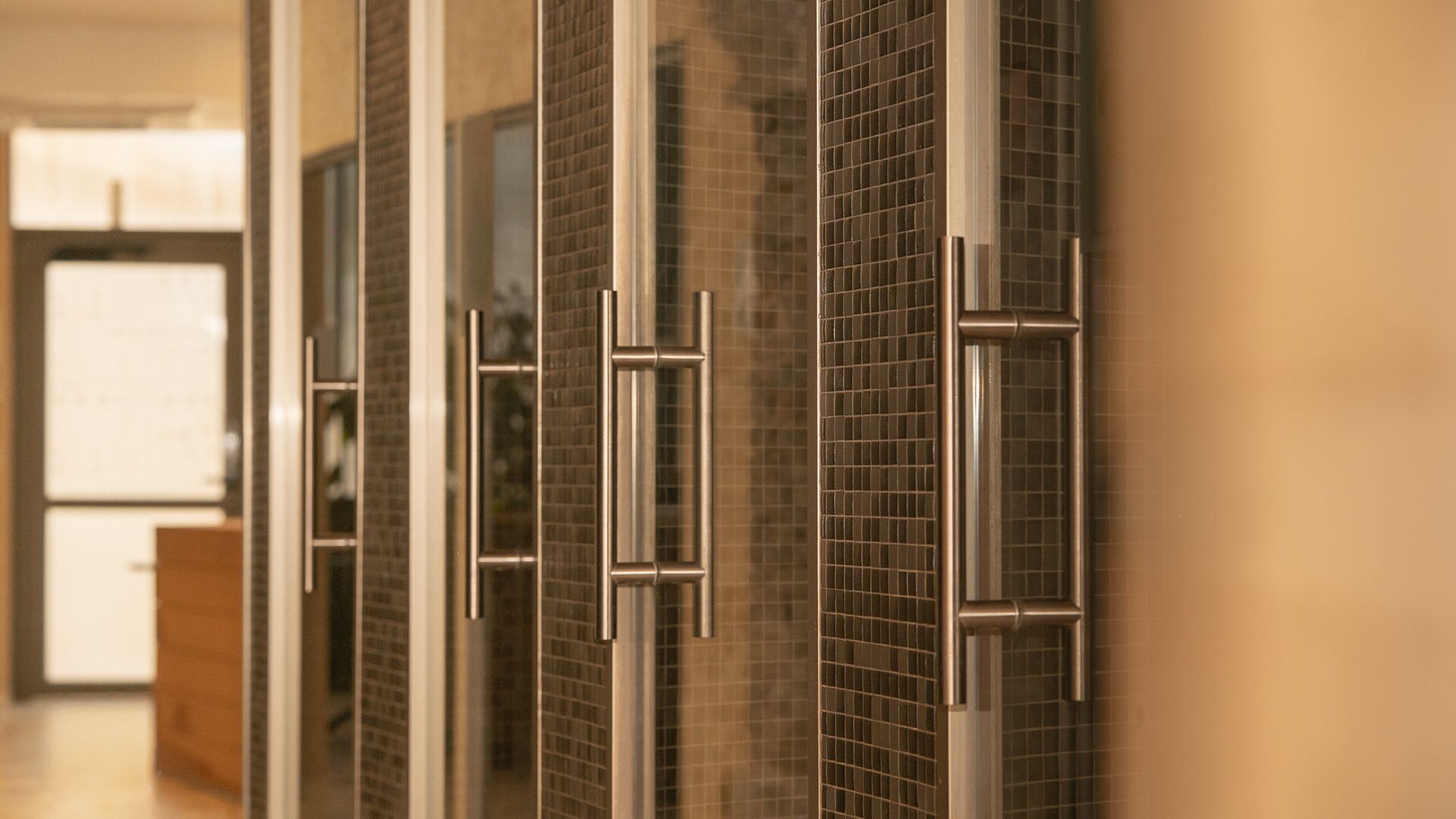 A corridor with glass doors and metal handles, leading to a room with a tiled wall.